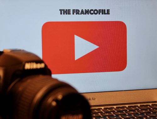 A Nikon camera in front of a computer screen showing the YouTube play button and "The Francofile."