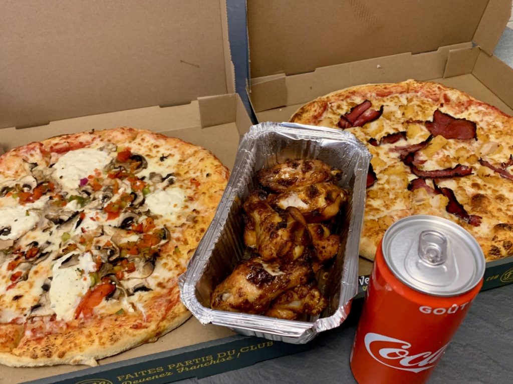 Two pizzas, a box of chicken wings, and a can of Coke.