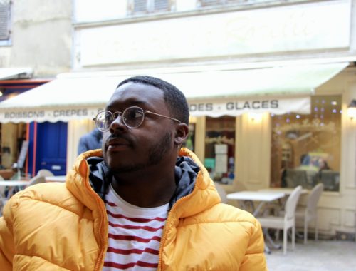 Jalen at a café in Troyes wearing a yellow jacket and red-striped shirt.