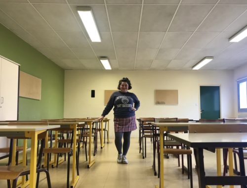 Maria standing among desks in an empty French classroom.