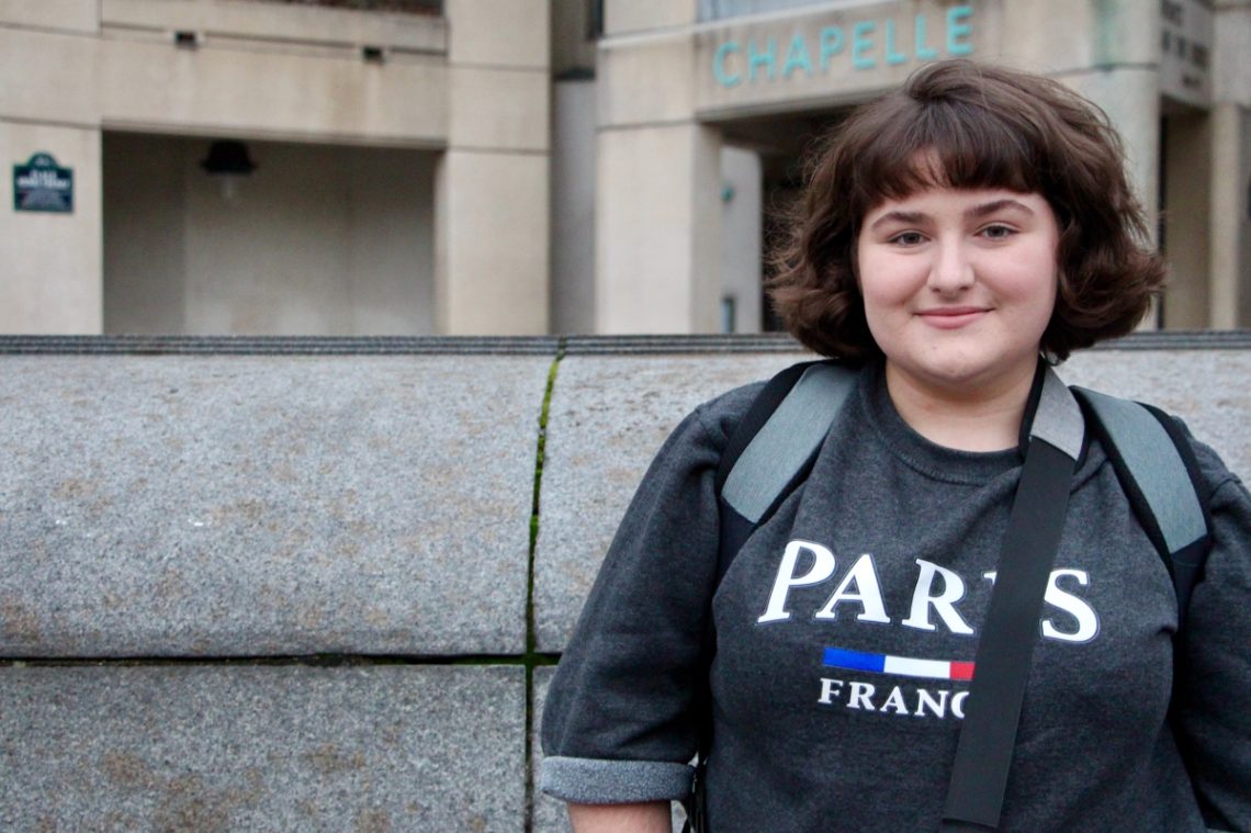 Maria smiling wearing a sweatshirt that says Paris, France.
