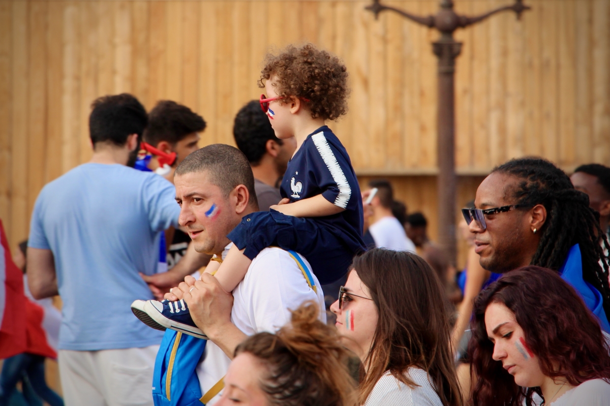 A boy sitting on a man's shoulders. Both sport French flag face paint.