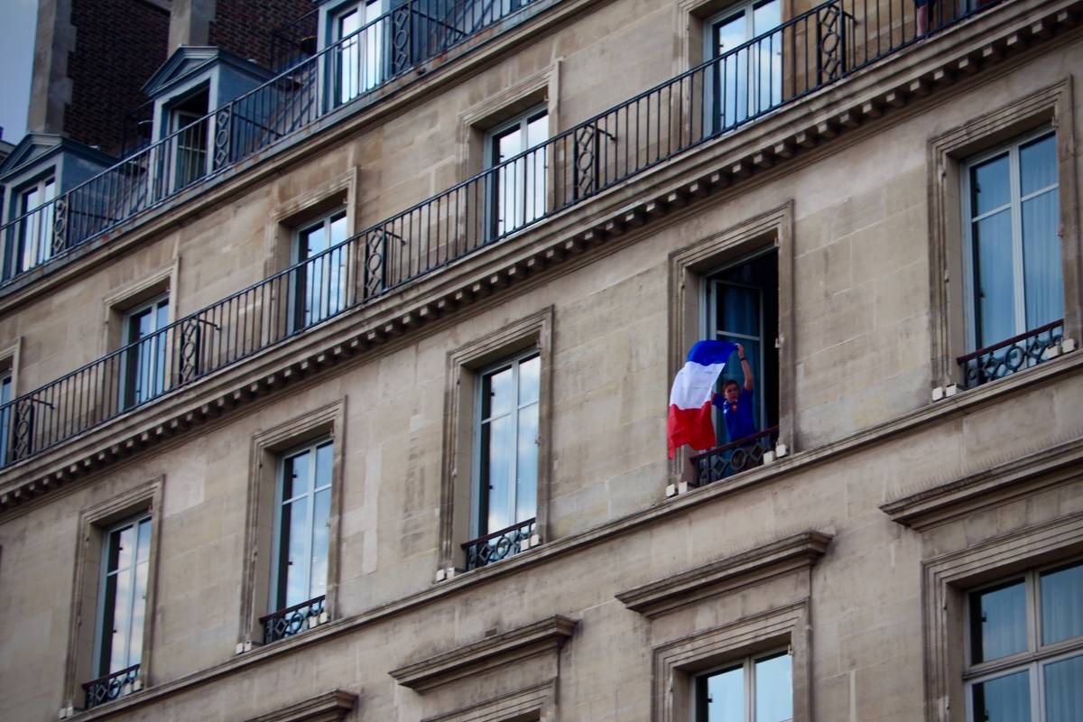 A boy waving a French flag out of an apartment window.