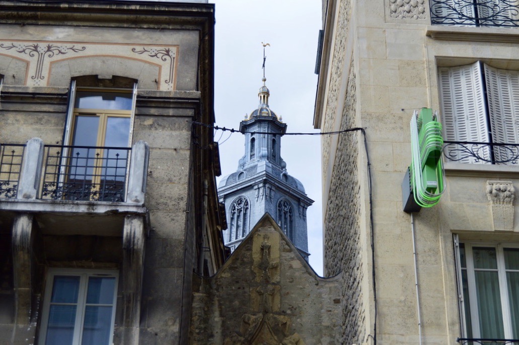 A blue tower peaking through two buildings in Reims, France.