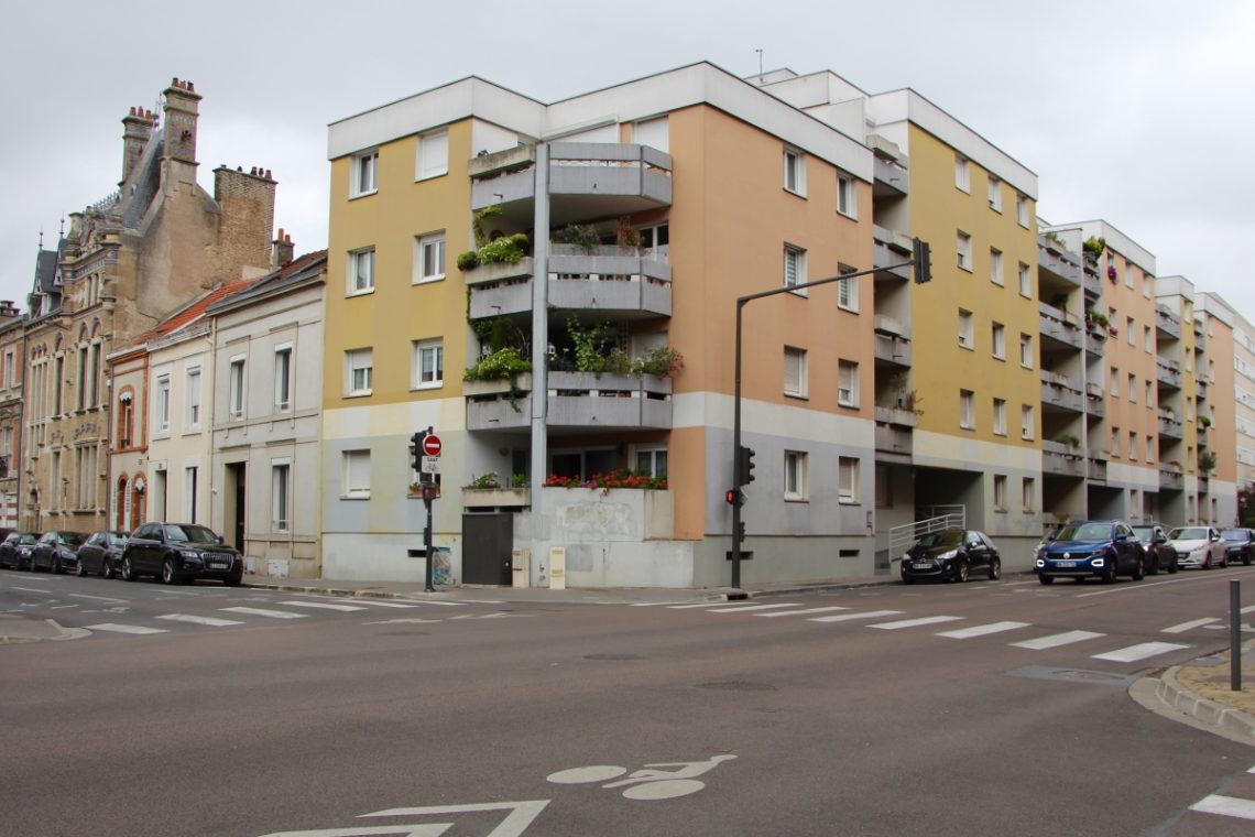 A view of a street corner in Reims, France with pastel pink and yellow buildings.