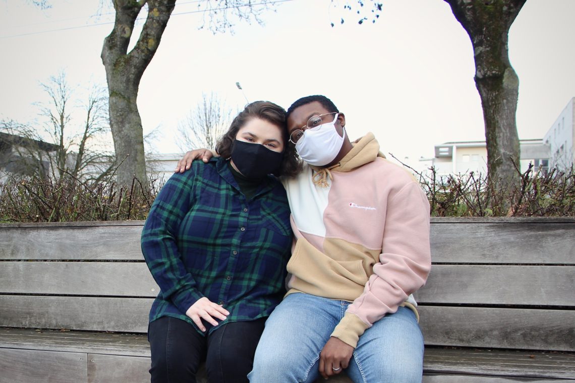 Maria and Jalen sit on a bench together, wearing masks, in Reims, France.