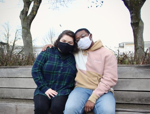 Maria and Jalen sit on a bench together, wearing masks, in Reims, France.