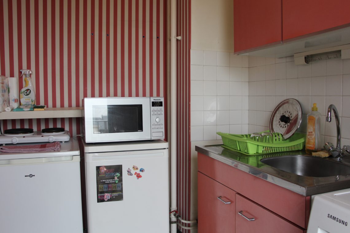 A view of a small apartment kitchen in Reims, France. The walls have striped pink wallpaper and the cabinets are pink.