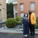 Maria and Jalen stand side by side in Reims, France with a bed of flowers and brick buildings behind them.