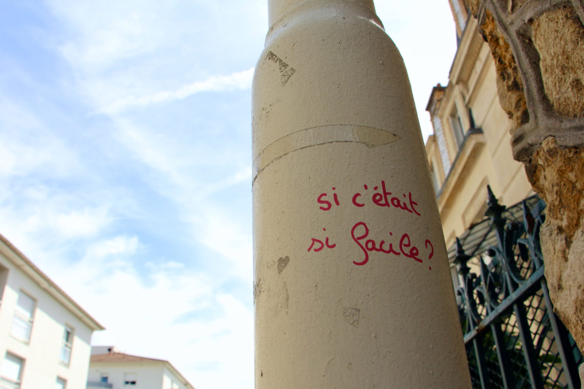 Red graffiti that reads Si c'était si facile? with a blue sky in the background.
