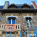 Art deco buildings in Nancy, France display a tattered fabric sign that reads L'HUMAIN AVANT LE PROFIT.