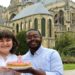 Jalen and Maria pose with a cake behind the Cathédrale de Reims.