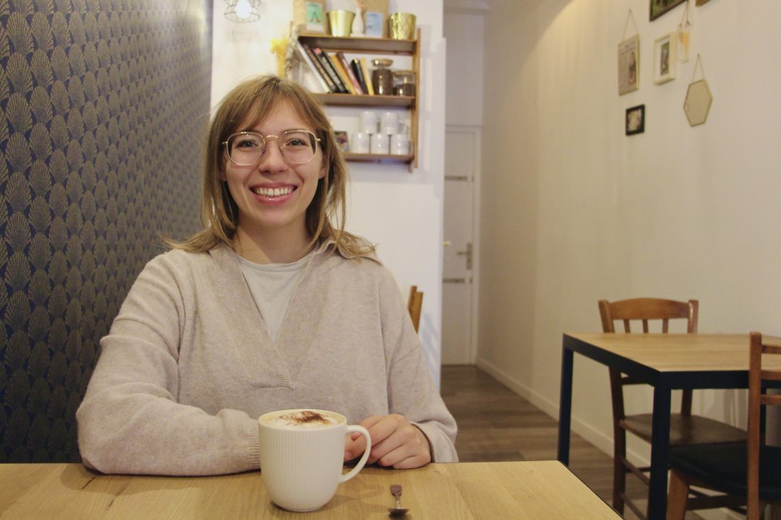Emma smiles with a cappuccino at Holy Shot Coffee Shop in Reims, France.