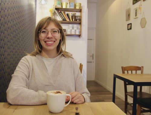 Emma smiles with a cappuccino at Holy Shot Coffee Shop in Reims, France.