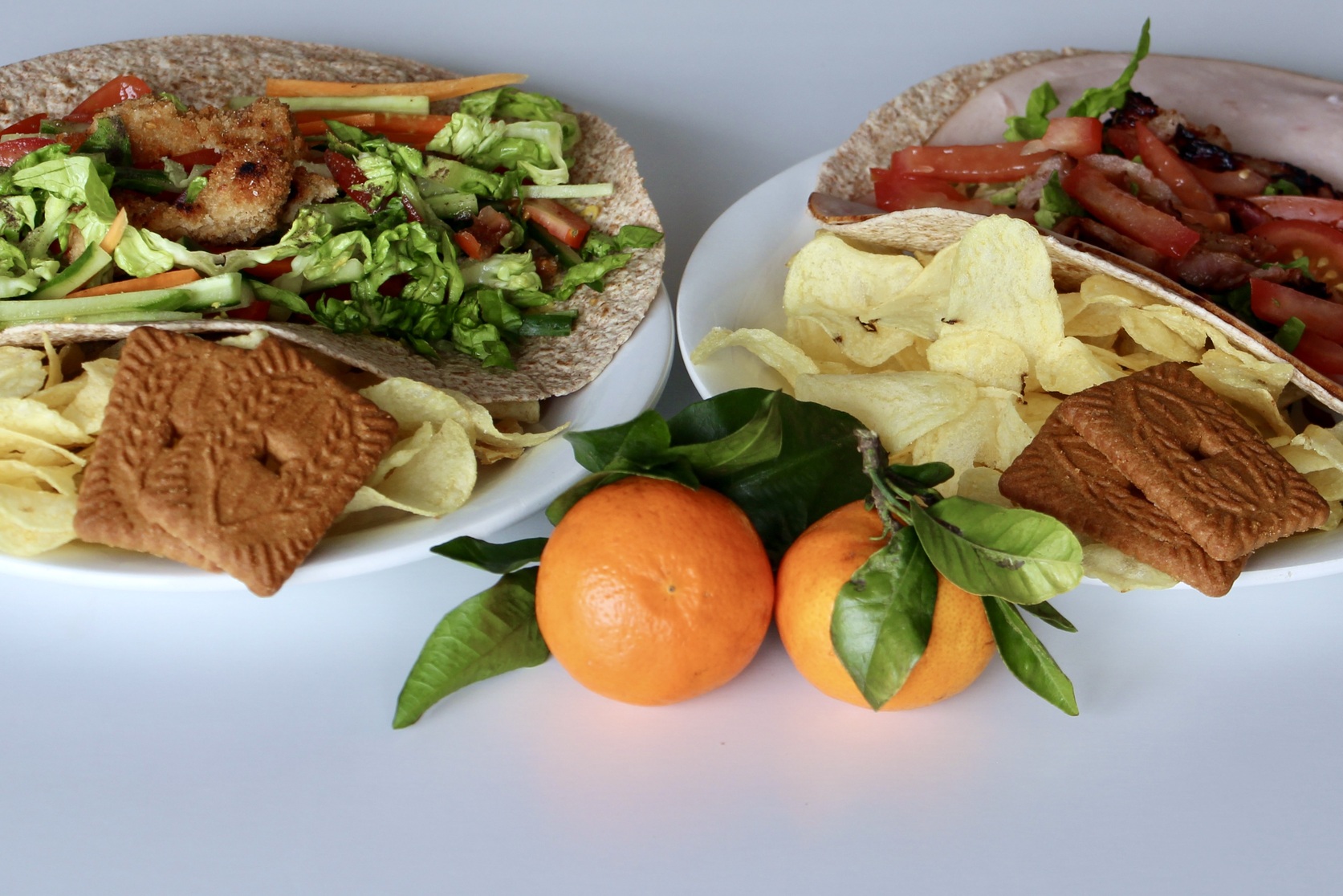 Two wraps with chips, cookies, and mandarine oranges on the side.