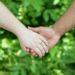 A close-up shot of Maria and Jalen holding hands with green plants in the background.