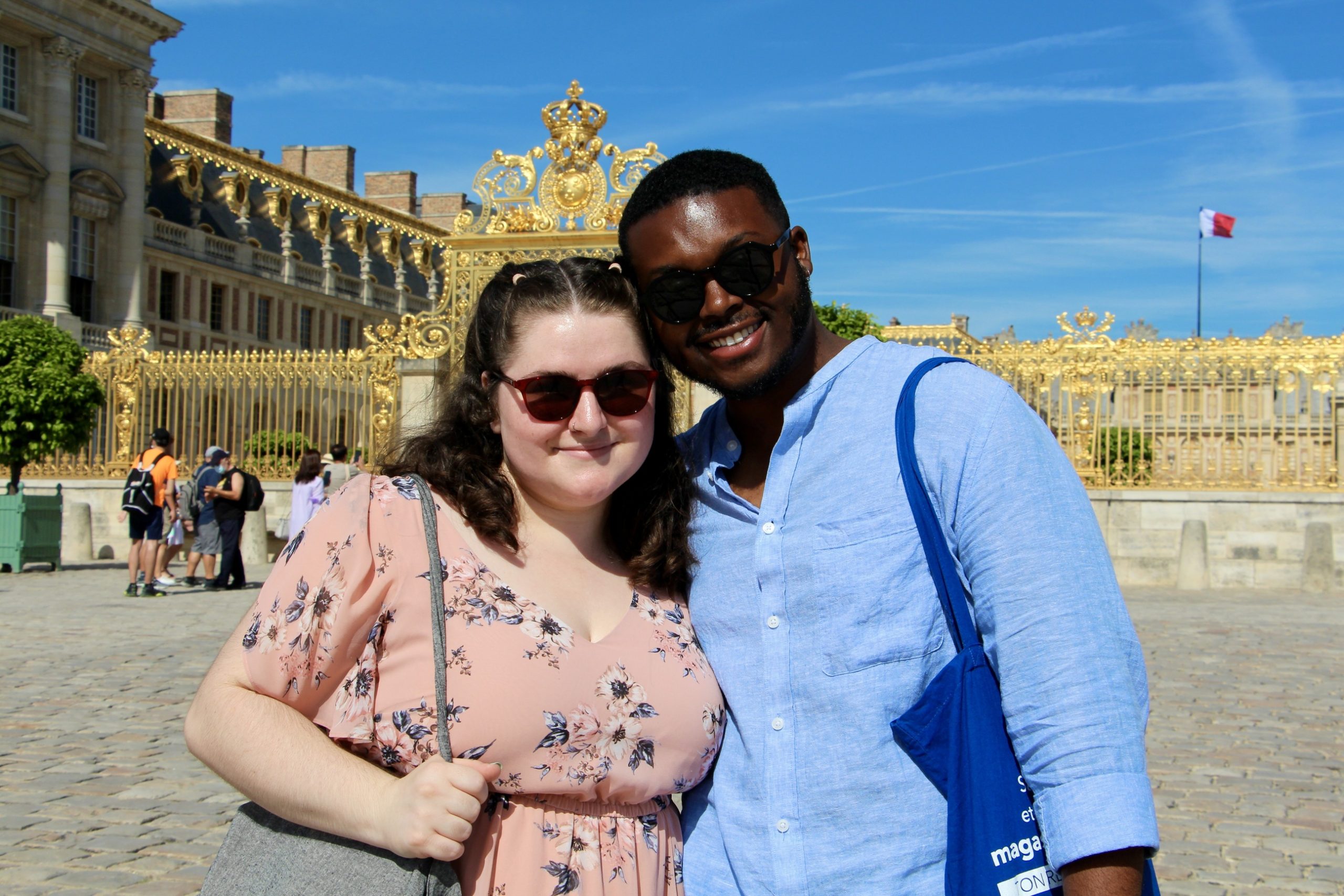 Jalen and Maria smile at the entrance gate of the Palace of Versailles.