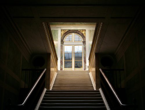 A bright stairwell contrasts with a dark room in the Palace of Versailles.