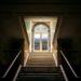 A bright stairwell contrasts with a dark room in the Palace of Versailles.