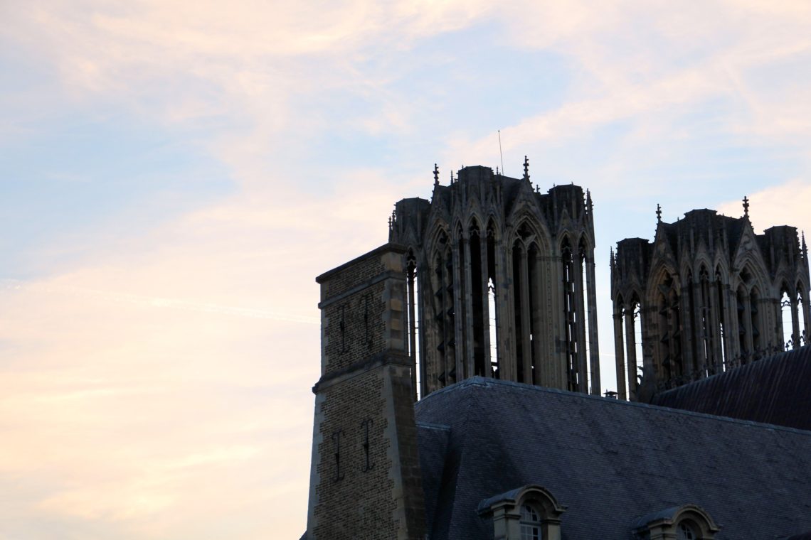The towers of the Cathédrale Notre-Dame de Reims against a soft orange and blue sky.