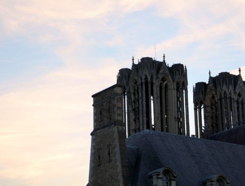 The towers of the Cathédrale Notre-Dame de Reims against a soft orange and blue sky.