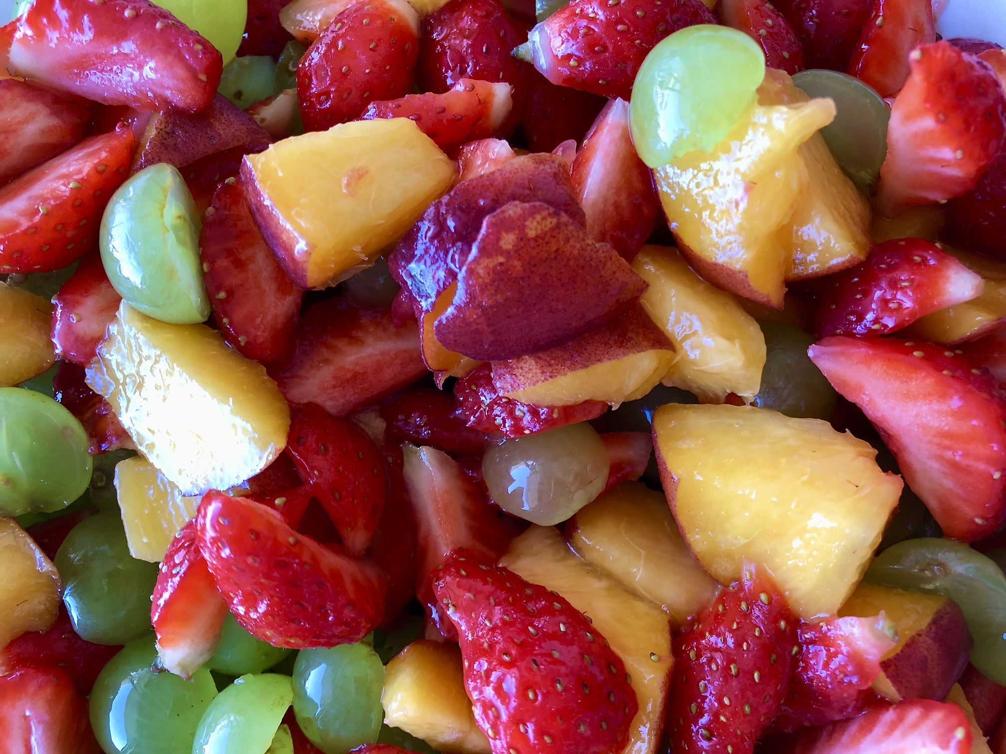 A close-up of fruit salad with strawberries, grapes, and peaches.