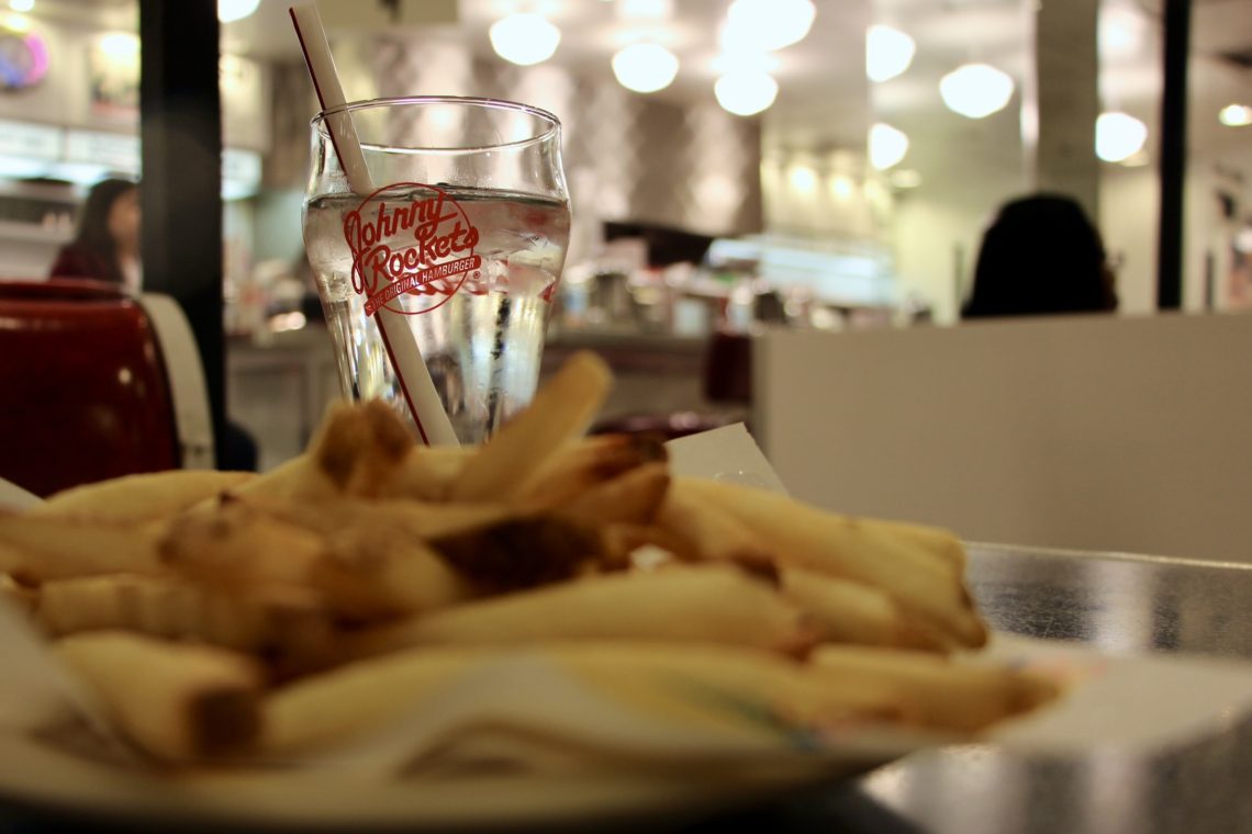 A plate of French fries and a glass with the Johnny Rockets logo.