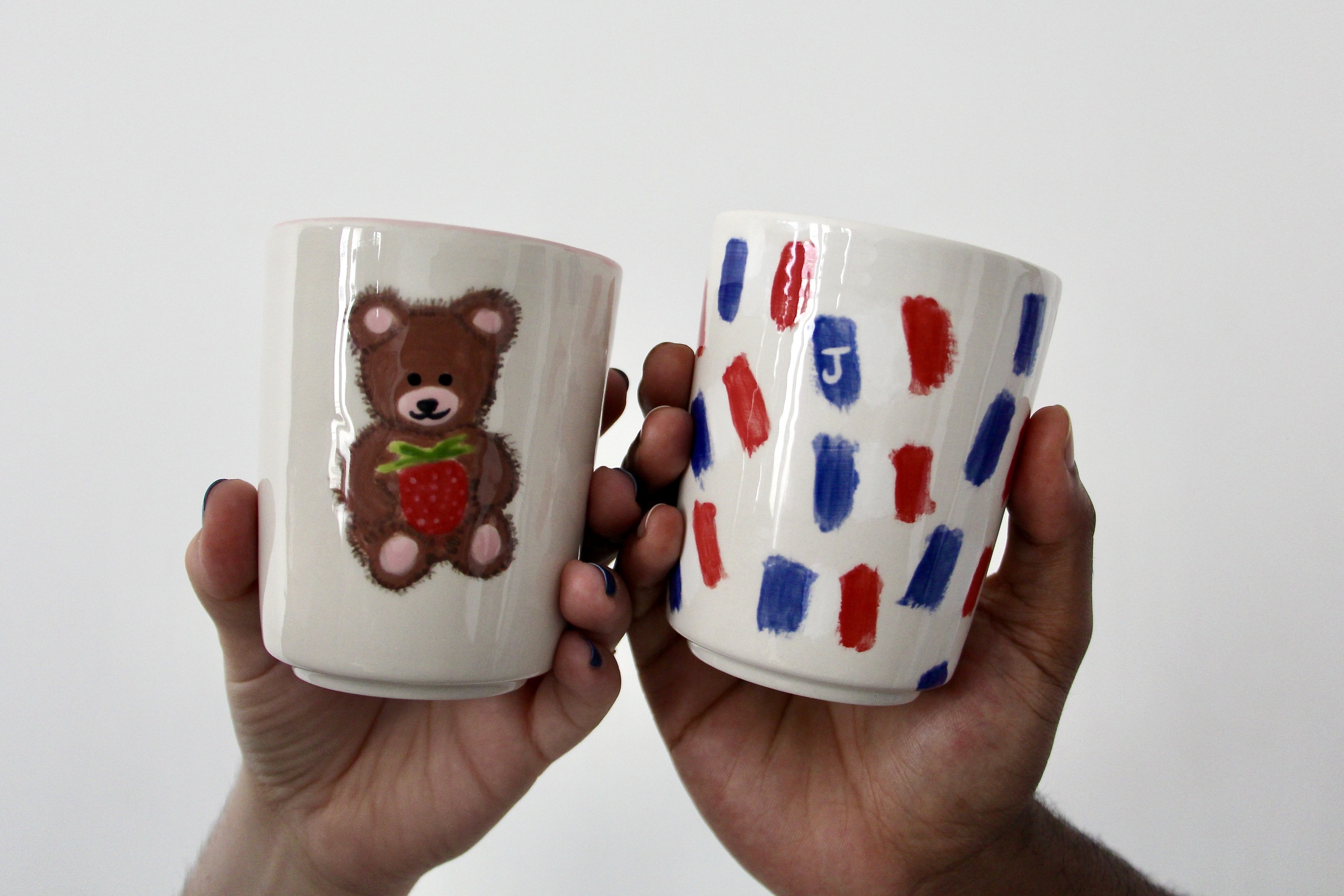 Holding our finished pottery pieces, one with a brown teddy bear holding a strawberry and one covered with French flags.